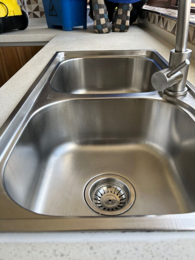 Aluminium sink being scrubbed to show kitchen deep cleaning benefits and hygiene improvement.